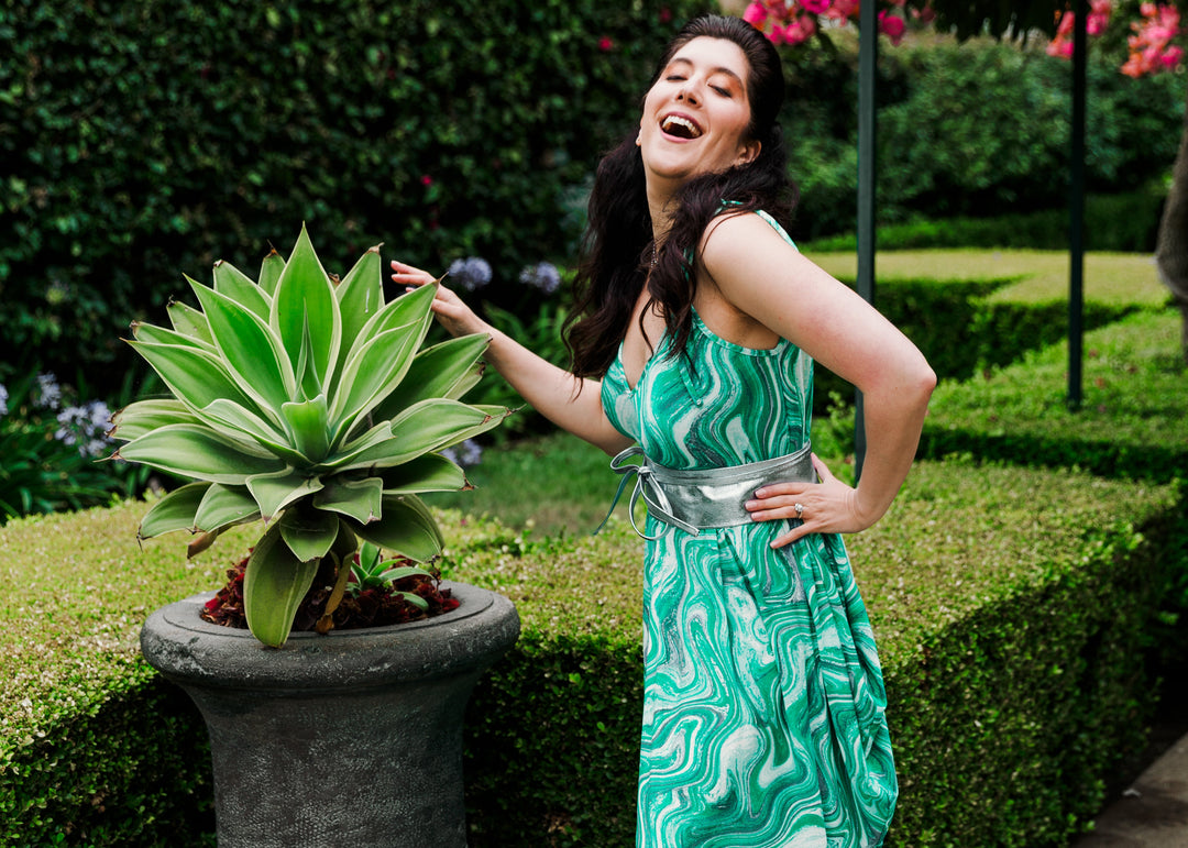 Woman in a green dress standing next to a potted plant in an outdoor setting