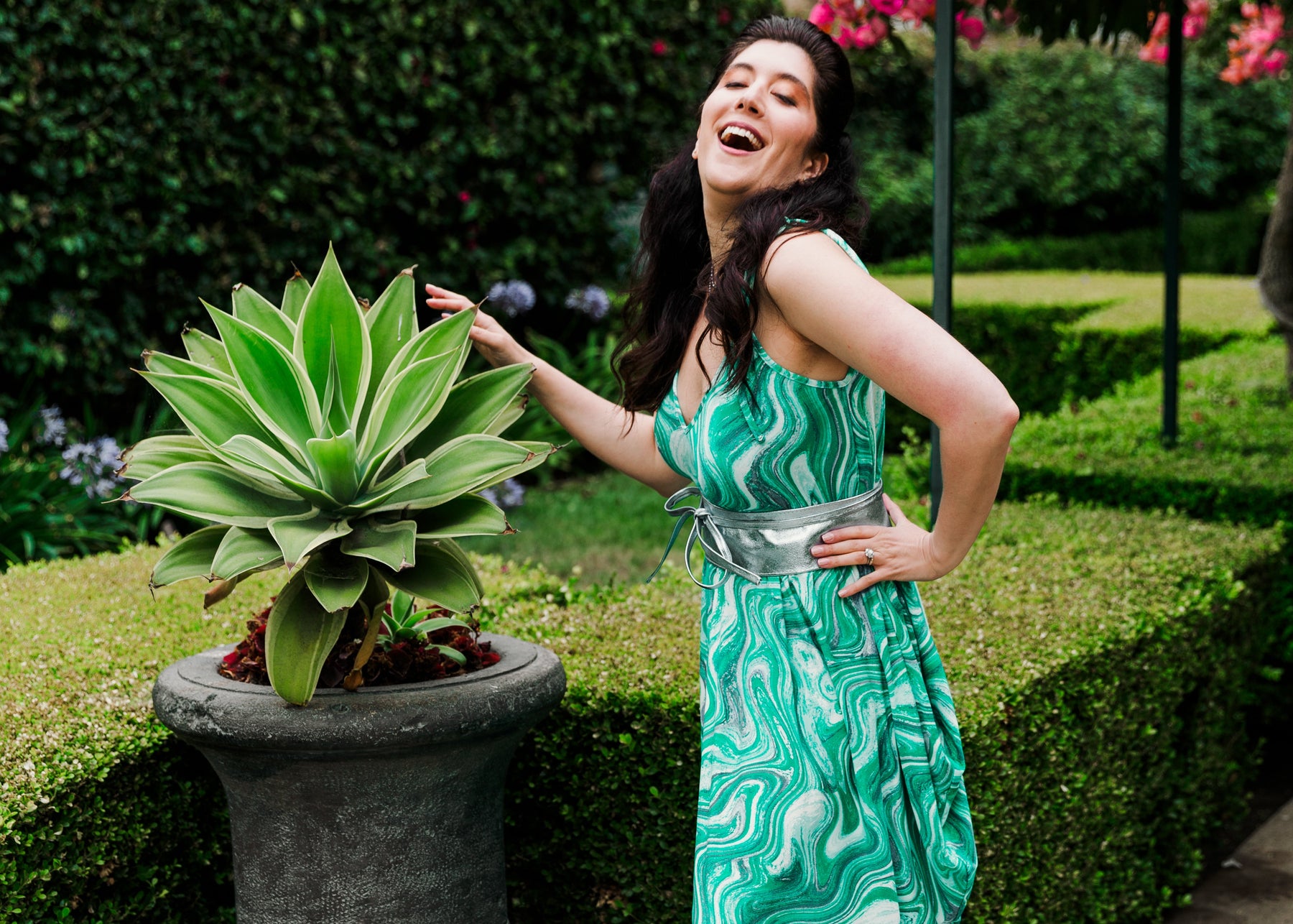 Woman in a green dress standing next to a potted plant in an outdoor setting